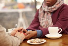 Two people supportively holding hands over coffee table