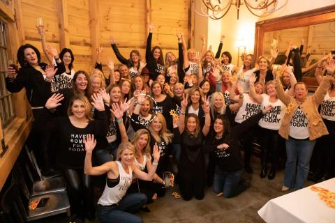 Large group of people wearing the same shirt, "Have some fun today" with their hands raised smiling for the photo.