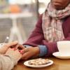 Two people supportively holding hands over coffee table Two people supportively holding hands over coffee table
